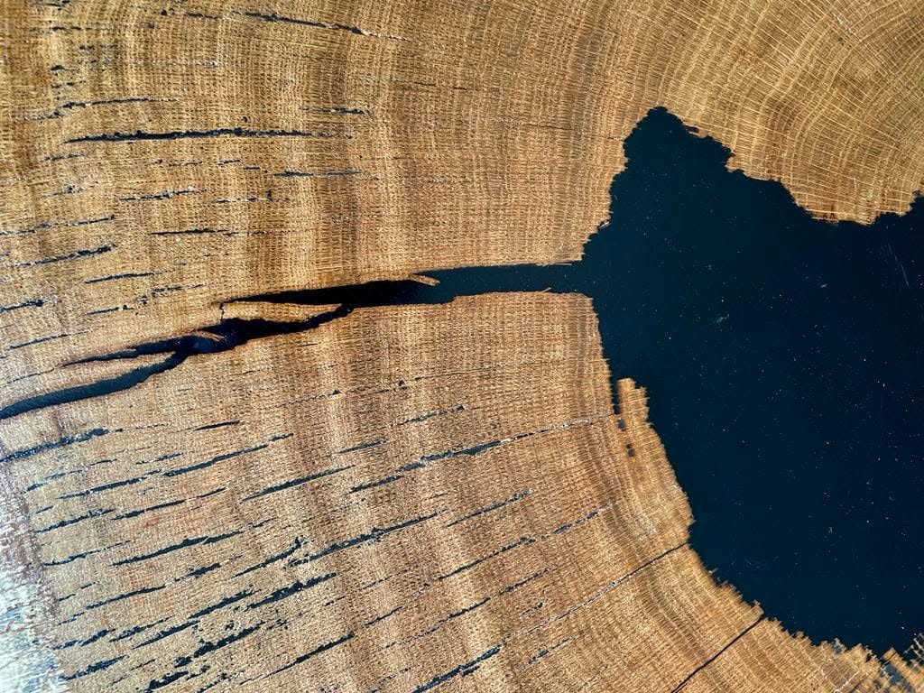 Zbliżenie na łączenie surowego drewna dębowego z głęboką, czarną żywicą epoksydową, wypełniającą naturalne pęknięcie w blacie.
